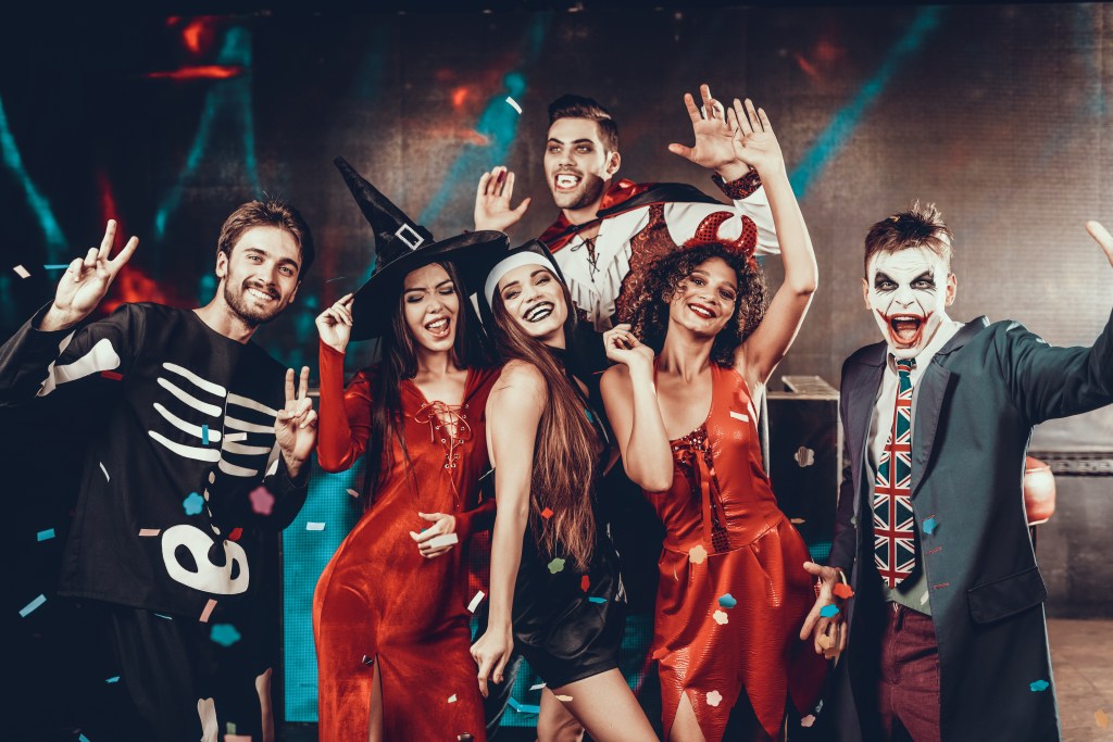 Group of young, smiling friends dressed in Halloween costumes, posing together in a nightclub